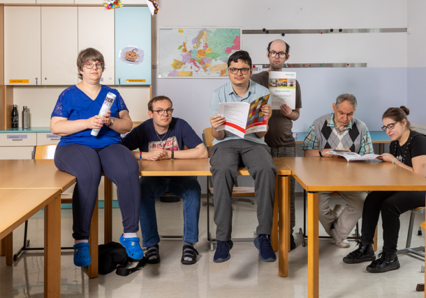 Das Fotos zeigt eine Gruppe in der Tagesstruktur Nobilegasse. Einige Personen lesen, andere halten Broschüren in die Kamera