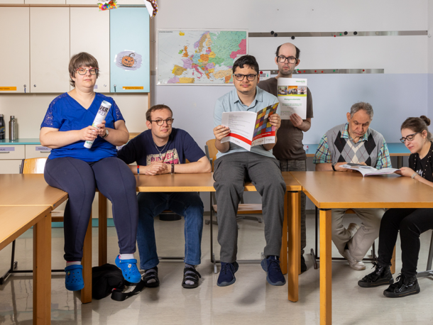 Das Fotos zeigt eine Gruppe in der Tagesstruktur Nobilegasse. Einige Personen lesen, andere halten Broschüren in die Kamera