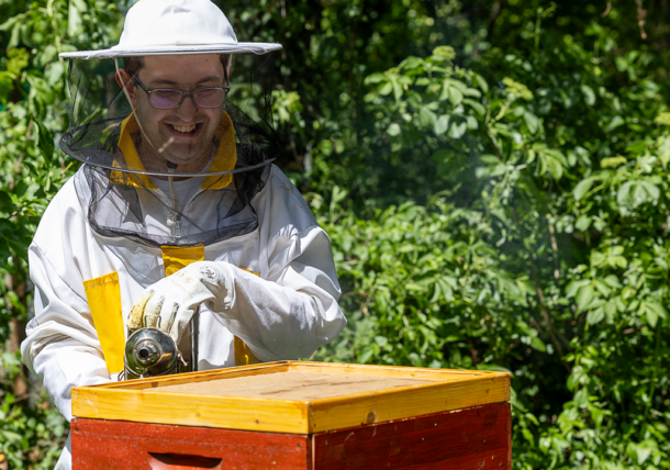 Ein Kunde mit Imkeranzug und Imkerhut arbeitet im Garten an einem Bienenstock.