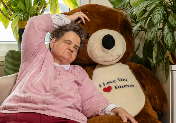 Eine Frau mit Sehschwaeche kuschelt sich an einen großen Teddybaeren.
