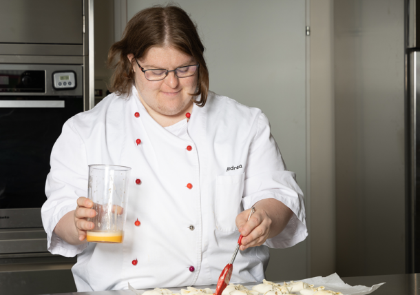 Eine Frau mit Downsyndrom bestreicht in einer Kueche der Lebenshilfe Wien mit einem Pinsel Blätterteiggebäck.