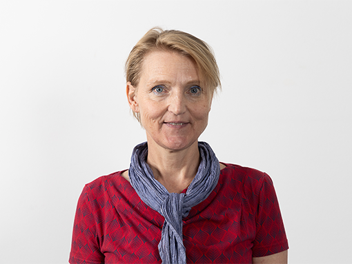 Die Mitarbeiterin Barbara Wazek schaut freundlich in die Kamera. Sie leitet die Tagesstruktur der Lebenshilfe Wien in der Dresdner Straße. Sie hat kurze blonde Haare, trägt ein rotes T-Shirt und ein blaues Halstuch.