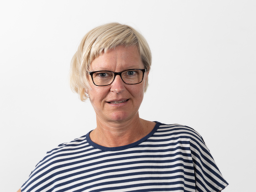 Die Mitarbeiterin Sandra Kaltenbrunner schaut in die Kamera. Sie leitet die Tagesstruktur der Lebenshilfe Wien in der Schuhfabrikgasse. Sie hat blonde kurze Haare, eine Brille und traegt ein blau-weiß gestreiftes T-Shirt.