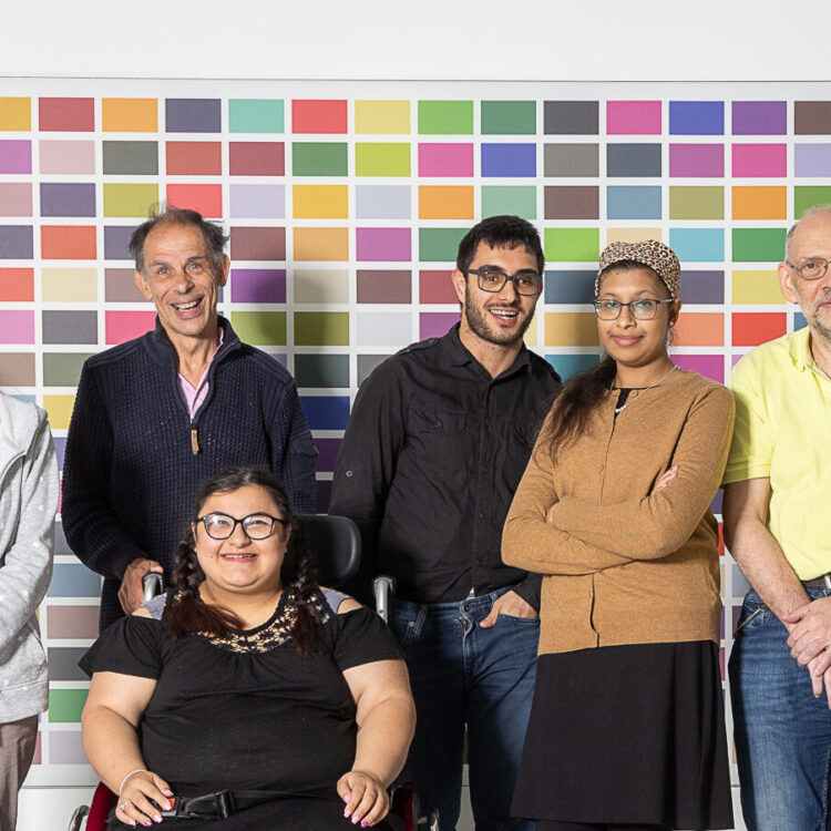 Das Foto zeigt ein Gruppenfoto des Mitsprache-Teams der Lebenshilfe Wien. Fünf Männer und drei Frauen mit Lernschwierigkeiten stehen vor einer bunten Wand, eine davon sitzt im Rollstuhl.