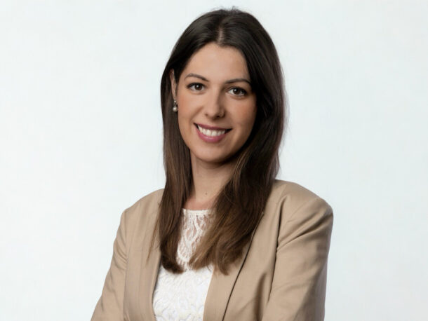Eine dunkelhaarige langhaarige Frau lächelt freundlich in die Kamera. Sie trägt einen beigen Blazer