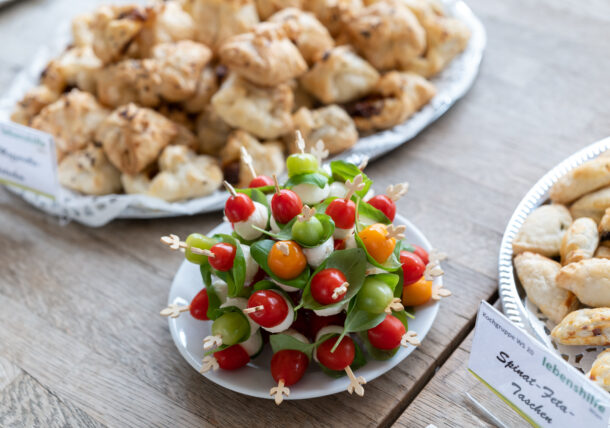 Das Foto zeigt kalte Häppchen, pikantes Fingerfood, dass die Kochgruppe der Lebenshilfe Wien zubereitet hat. Man sieht Spieße mit Mozzarella und Tomaten sowie gefüllte Blätterteigtaschen auf einen Tisch stehen.
