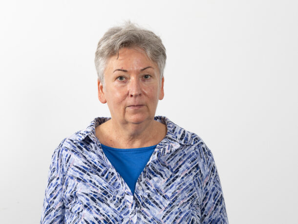 Das Foto zeigt unsere Freiwilligen-Koordinatorin Anna Haider. Sie ist eine Frau mittleren Alters mit kurzen grauen Haaren und trägt eine blau gemusterte Bluse.