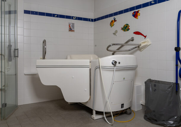 Auf dem Foto sieht man eine Pflegebadewanne in einem Badezimmer. An den Fliesen an der Wan kleben über der Wanne bunte Fische.