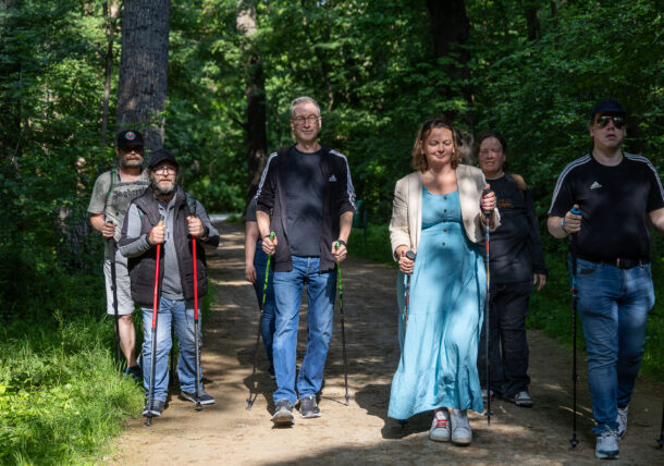 Eine Personengruppe geht mit Nordic Walking Stöcken durch einen Wald.