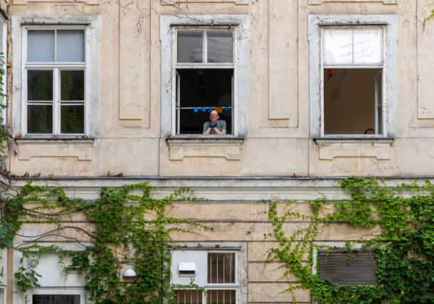 Das Foto zeigt drei Fenster der Tagesstruktur in der Schottengasse in einem Altbaugebauede. Aus dem mittleren Fenster schaut ein Mann mit Brille. Die Hauswand ist mit grünem Efeu bewachsen