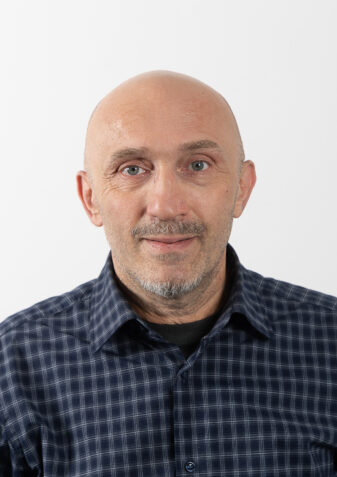 Der Mitarbeiter Giorgi Gochaleishvili schaut freundlich in die Kamera. Er leitet die Wohngemeinschaft der Lebenshilfe Wien in der Rinnböckstraße. Er hat keine Haare, trägt ein blaues kariertes Hemd und hat einen grauen Bart.