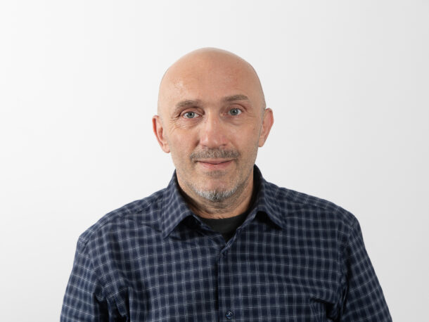 Der Mitarbeiter Giorgi Gochaleishvili schaut freundlich in die Kamera. Er leitet die Wohngemeinschaft der Lebenshilfe Wien in der Rinnböckstraße. Er hat keine Haare, trägt ein blaues kariertes Hemd und hat einen grauen Bart.