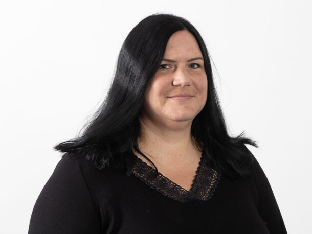 Die Mitarbeiterin Michaela Mayr schaut freundlich in die Kamera. Sie ist fuer den Bereich Gesundheit und Pflege in der Lebenshilfe Wien verantwortlich. Sie hat lange schwarze Haare und trägt ein dunkles Oberteil.