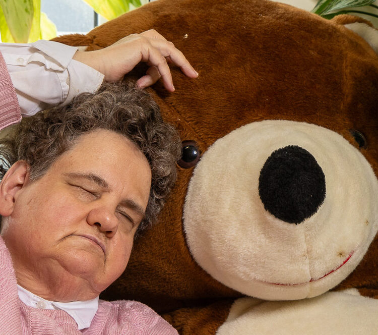 Eine blinde, ältere Frau kuschelt sich an einen großen Teddybären.