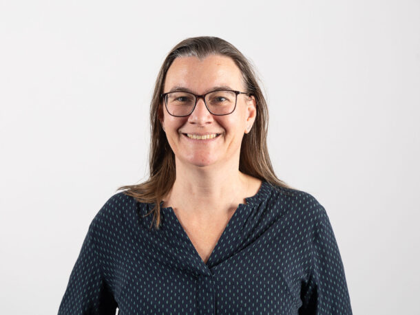 Die Mitarbeiterin Sonja Abel lächelt freundlich in die Kamera. Sie ist fuer den Bereich Unterstützte Kommunikation in der Lebenshilfe Wien. Sie hat eine Brille und trägt ein dunkles Oberteil.