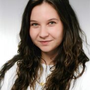 Eine junge Frau mit langen dunklen Haaren sieht freundlich in die Kamera. Sie trägt eine weiße Bluse.