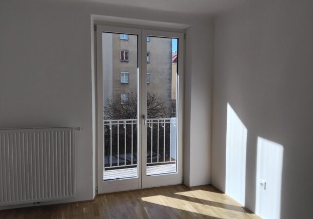 Man sieht einen Auschnitt einer neuen Wohnung. Durch die Balkontüre scheint die Sonne. Alles sieht sauber aus, auch der neue Parkettboden