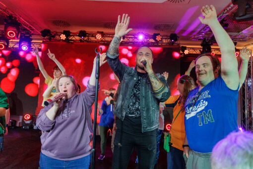 Das Foto zeigt einen Schlagersänger mit zwei Kunden der Lebenshilfe Wien, die gemeinsam auf der Bühne singen.