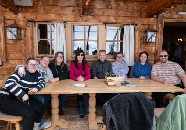 Eine Personengruppe sitzt an einem Tisch vor einer Holzwand, die zu einer Hütte in Gurgl gehört