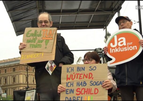 Drei Personen protestieren vor dem Parlament in Wien. Sie halten Schilder mit ihren Forderungen in die Höhe