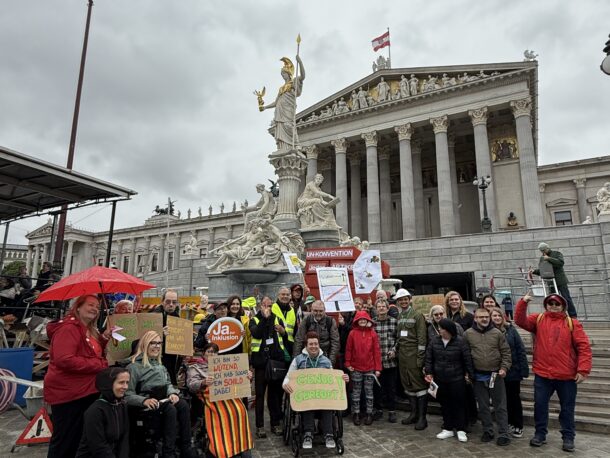 Eine Gruppe von Menschen mit und ohne Behinderungen protestiert vor dem Parlament in Wien. Die Aktion heißt BAUSTELLE INKLUSION