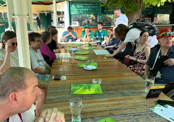 Eine Personengruppe sitzt an einem Tisch in einem schattigen Biergarten zusammen