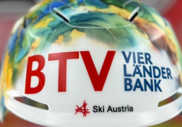 Nahaufnahme eines weißen Sporthelms mit bunten abstrakten Motiven und dem fetten Text BTV VIER LÄNDER BANK und Ski Austria auf der Vorderseite.