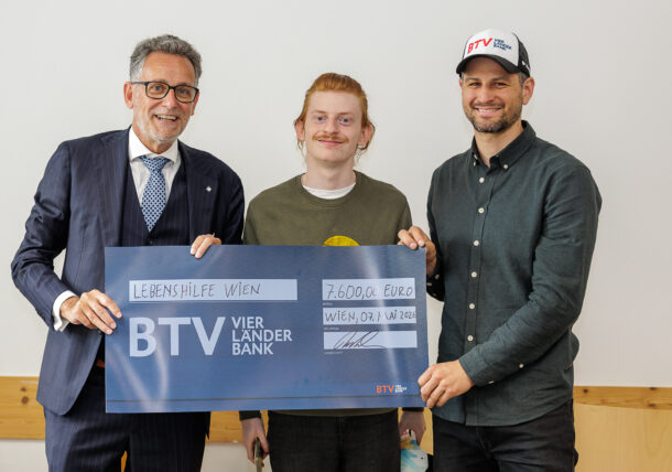 Drei Männer lächeln und halten einen großen, feierlichen Scheck der BTV Bank über 7.600 Euro, ausgestellt auf die Lebenshilfe Wien. Der Mann rechts trägt eine BTV-Mütze, der mittlere Mann hat rötliche Haare und einen Schnurrbart.