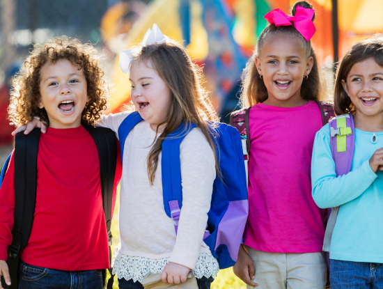 Vier Kinder mit Rucksäcken, die draußen lächeln und lachen.