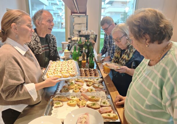 Eine Gruppe von Menschen, die um einen Buffettisch herumsteht, auf dem Tabletts mit Hors d’oeuvres und Vorspeisen stehen.
