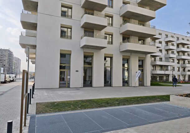 Modernes weißes Mehrfamilienhaus mit mehreren Balkonen und verglasten Eingängen im Erdgeschoss; in der Nähe des Gebäudes befindet sich ein Schild der Lebenshilfe.