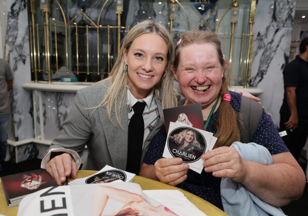 Die Sängerin Charlien lächelt neben einem Fan, der eine Sammlung ihrer Werbeaufkleber und Fotos in der Hand hält.